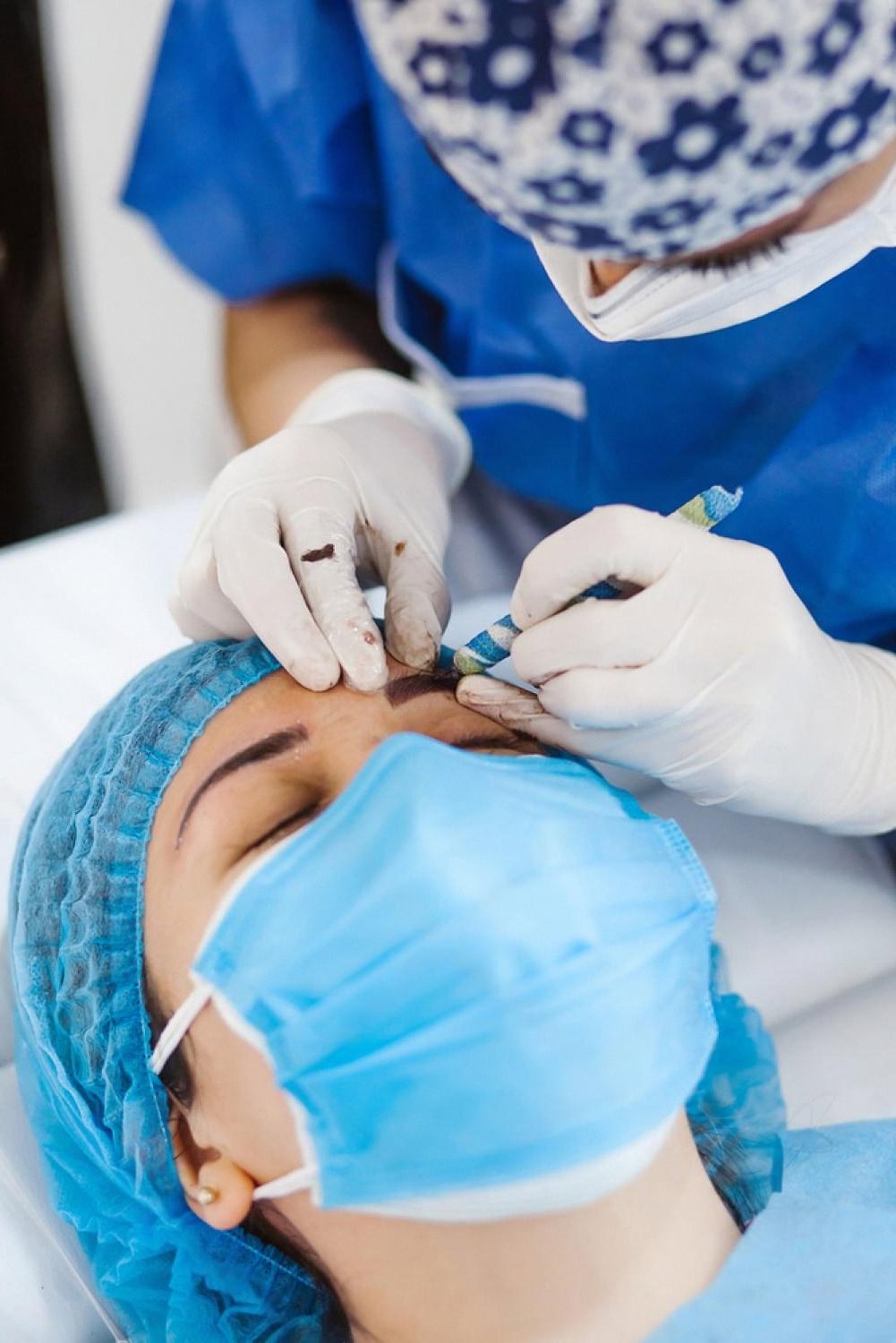 Technician performing microblading strokes on a client's eyebrow using a hand tool