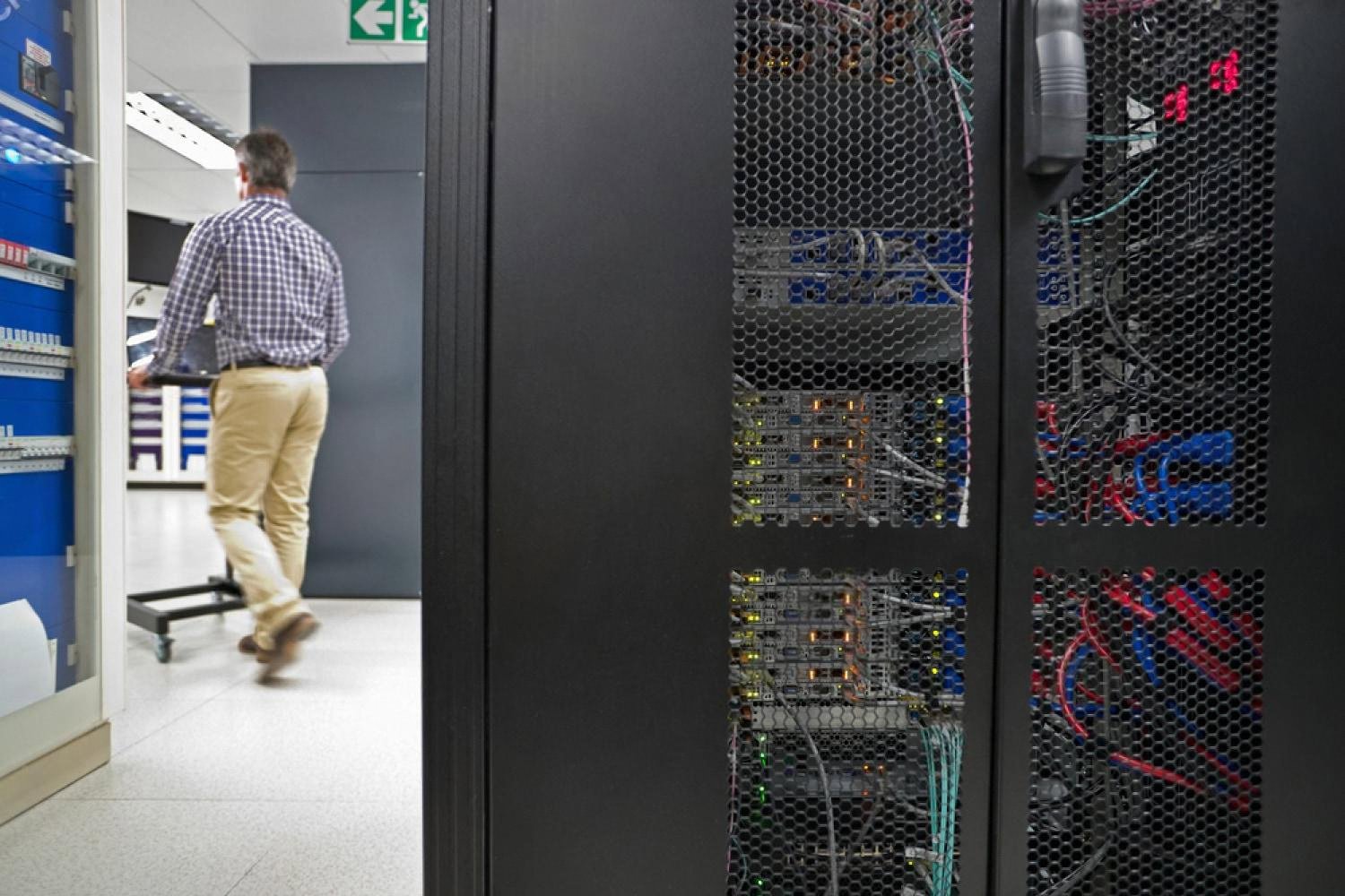 Technician walking past open server racks in a UAE data centre used for business web hosting